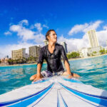 Serene surfer sitting on surfboard in Honolulu waters with city skyline backdrop.