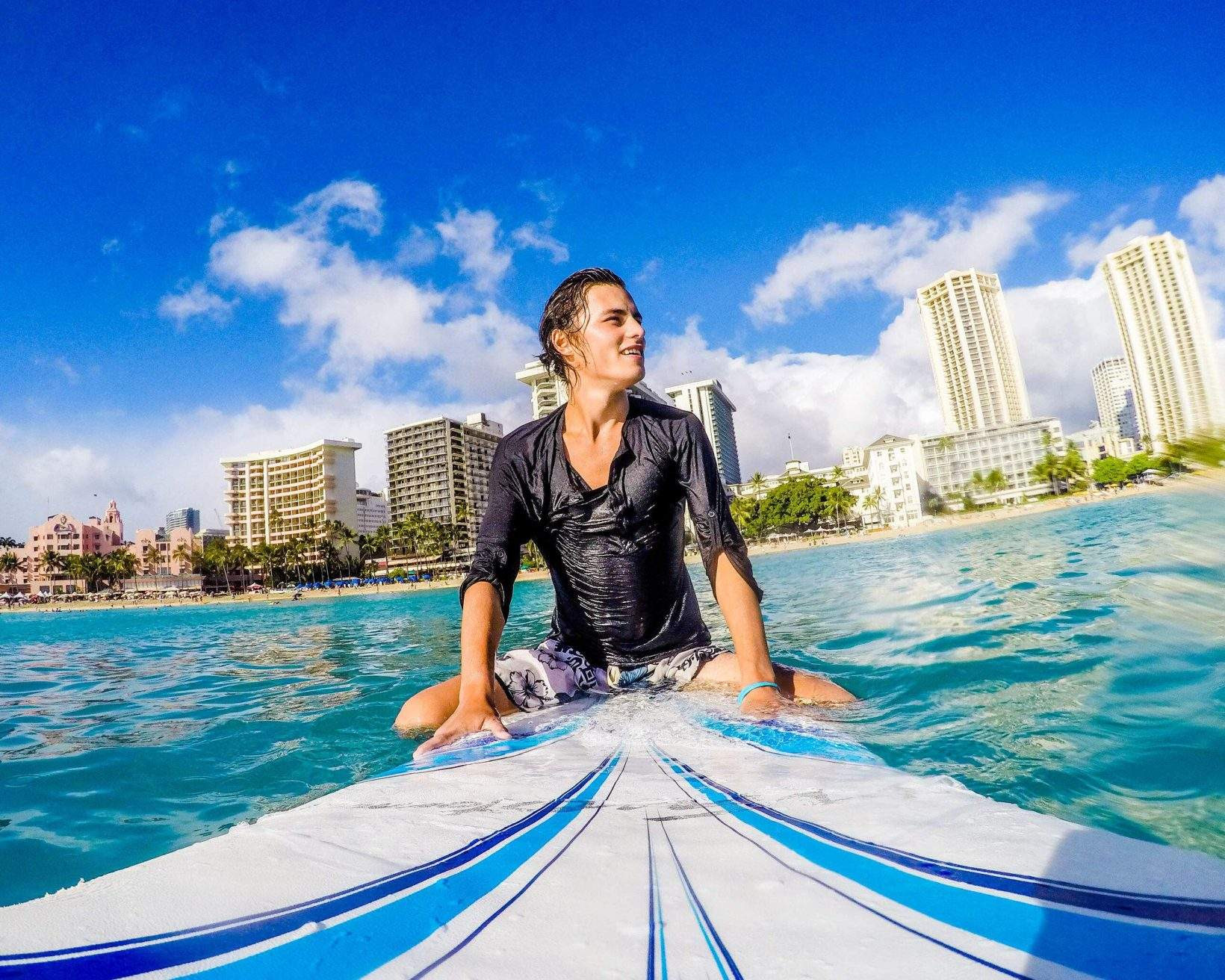 Serene surfer sitting on surfboard in Honolulu waters with city skyline backdrop.