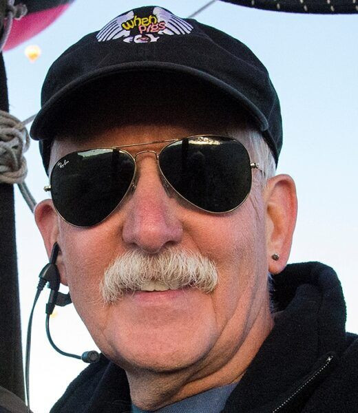 Doug Gantt smiles warmly next to his inflated pig-shaped hot air balloon, Ham-Let, at a balloon festival.