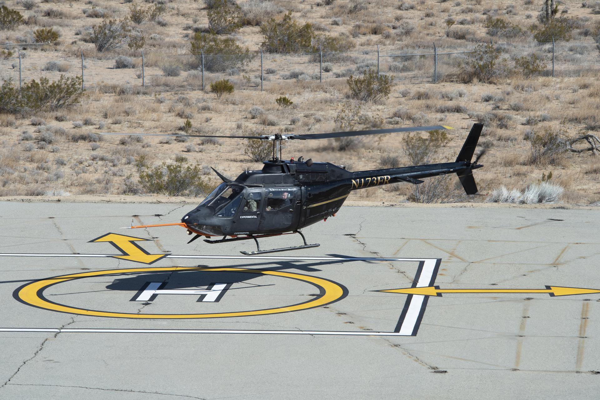 A helicopter takes off vertically from a desert landscape, showcasing its rotor blades and landing gear.