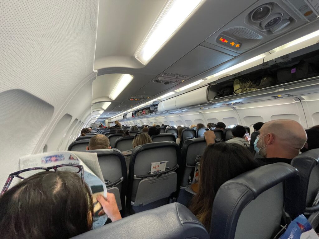 Interior view of an Allegiant Airbus A319 cabin filled with passengers, showcasing rows of gray seatbacks.