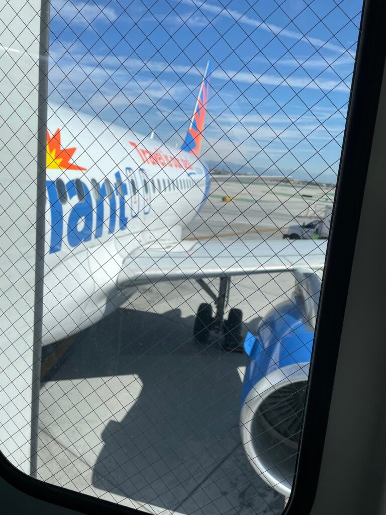 Allegiant Airbus A319 parked at the gate, as seen from the airport terminal window.