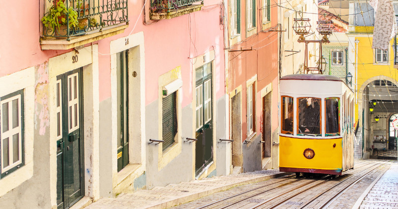 A yellow tram climbing a hill in Lisbon, passing colorful traditional buildings