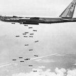 Boeing B-52 Stratofortress bombing Vietnam, alt text: A Boeing B-52 Stratofortress bomber releases a stream of bombs over Vietnam during the Vietnam War, showcasing its bombing capabilities.