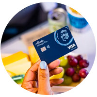 An Alaska Airlines credit card, emphasizing triple mile rewards for international flight bookings.