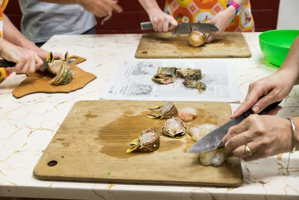 Three pairs of hands expertly chopping raw lobster, still in its shell, during a Cuban cooking class.