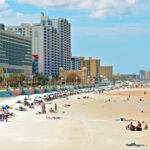 Daytona Beach under clear skies during the day, showcasing its beautiful coastline and inviting atmosphere for visitors arriving via nearby airports.