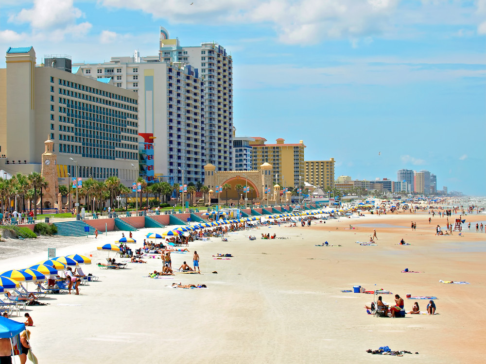 Daytona Beach under clear skies during the day, showcasing its beautiful coastline and inviting atmosphere for visitors arriving via nearby airports.