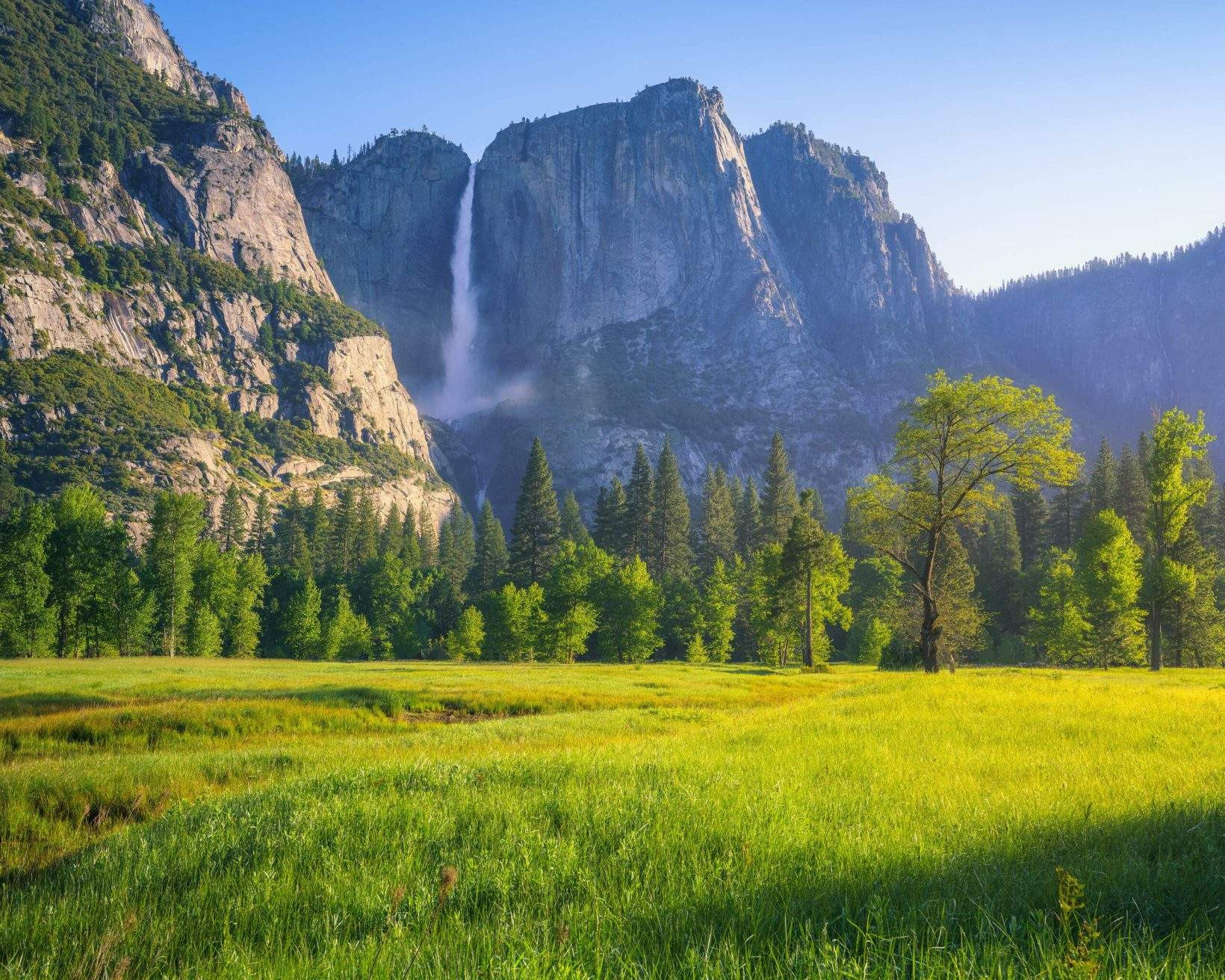 Yosemite Valley with lush green trees and a waterfall cascading down the granite cliffs in the background.