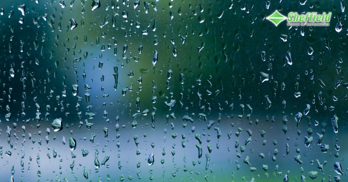 Raindrops on a plane window, blurring the outside view of green and blue objects, related to the question of whether rain cancels flights.