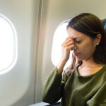 Woman pinching nose on plane, illustrating sinus pressure during flight with a sinus infection.