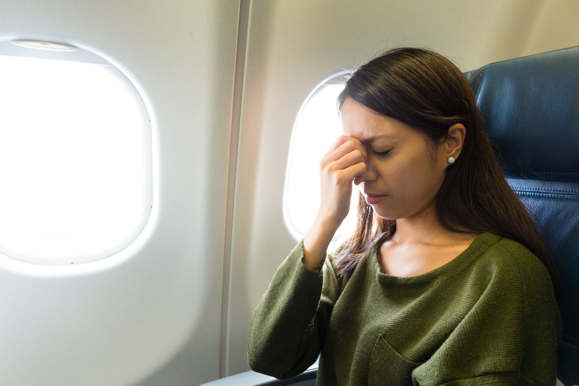 Woman pinching nose on plane, illustrating sinus pressure during flight with a sinus infection.