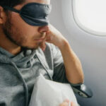 A man resting on the plane with an eye mask covering his eyes.