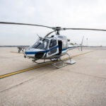 White helicopter awaiting passengers near airplane tails at Milan Malpensa Airport