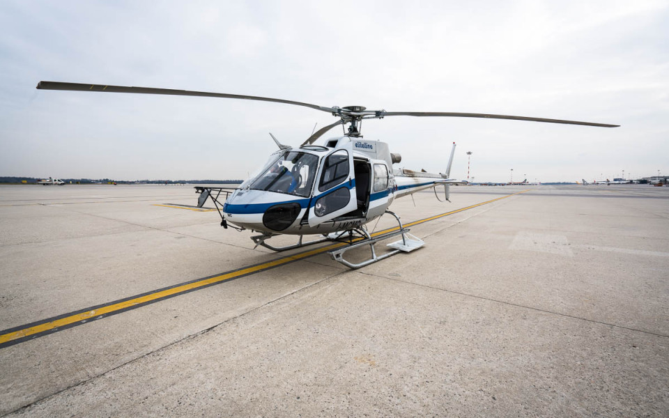 White helicopter awaiting passengers near airplane tails at Milan Malpensa Airport