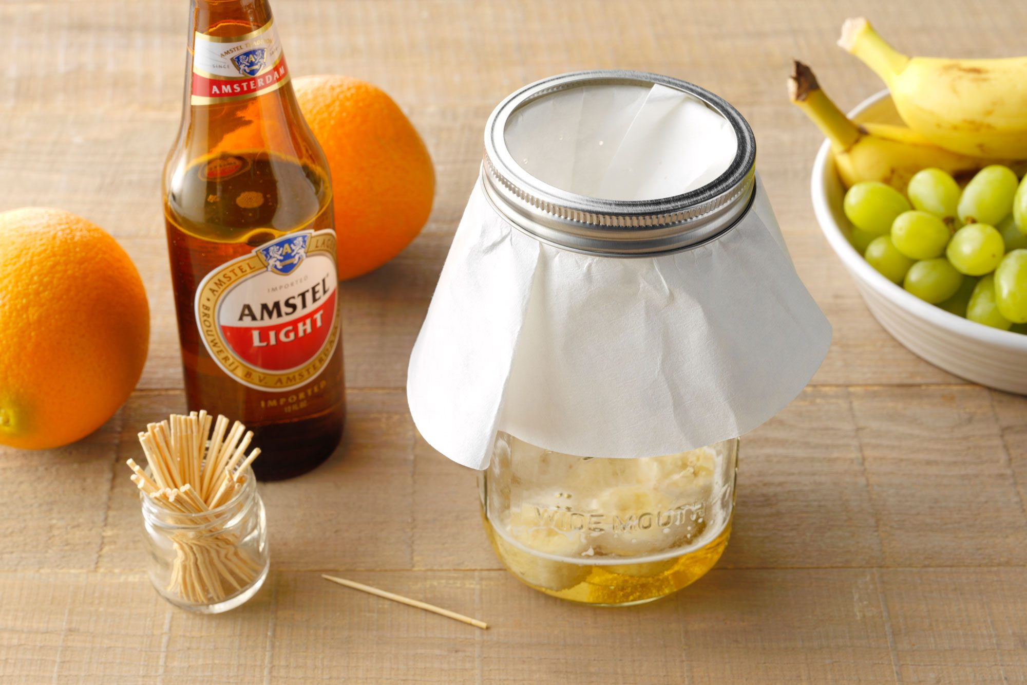 trap 5 set up in a glass jar with toothpicks, bottle of beer, and fresh fruit nearby on wooden surface