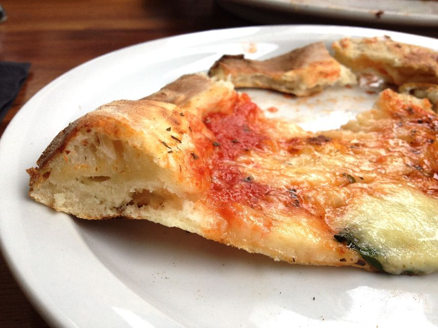 Pizza slice being held up to show thin and chewy undercrust