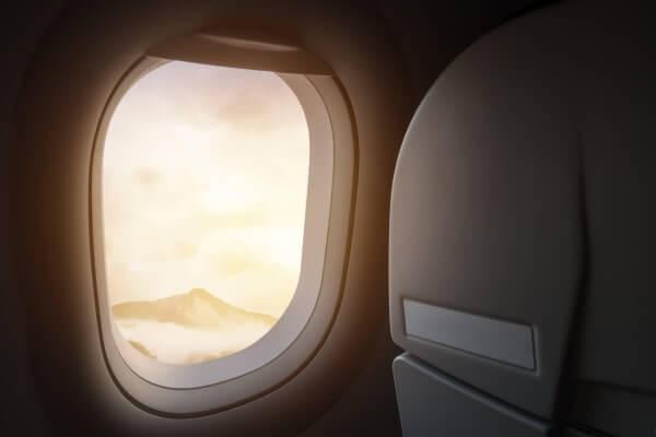 An airplane is visible through an airplane window, with mountains seen in the distance.