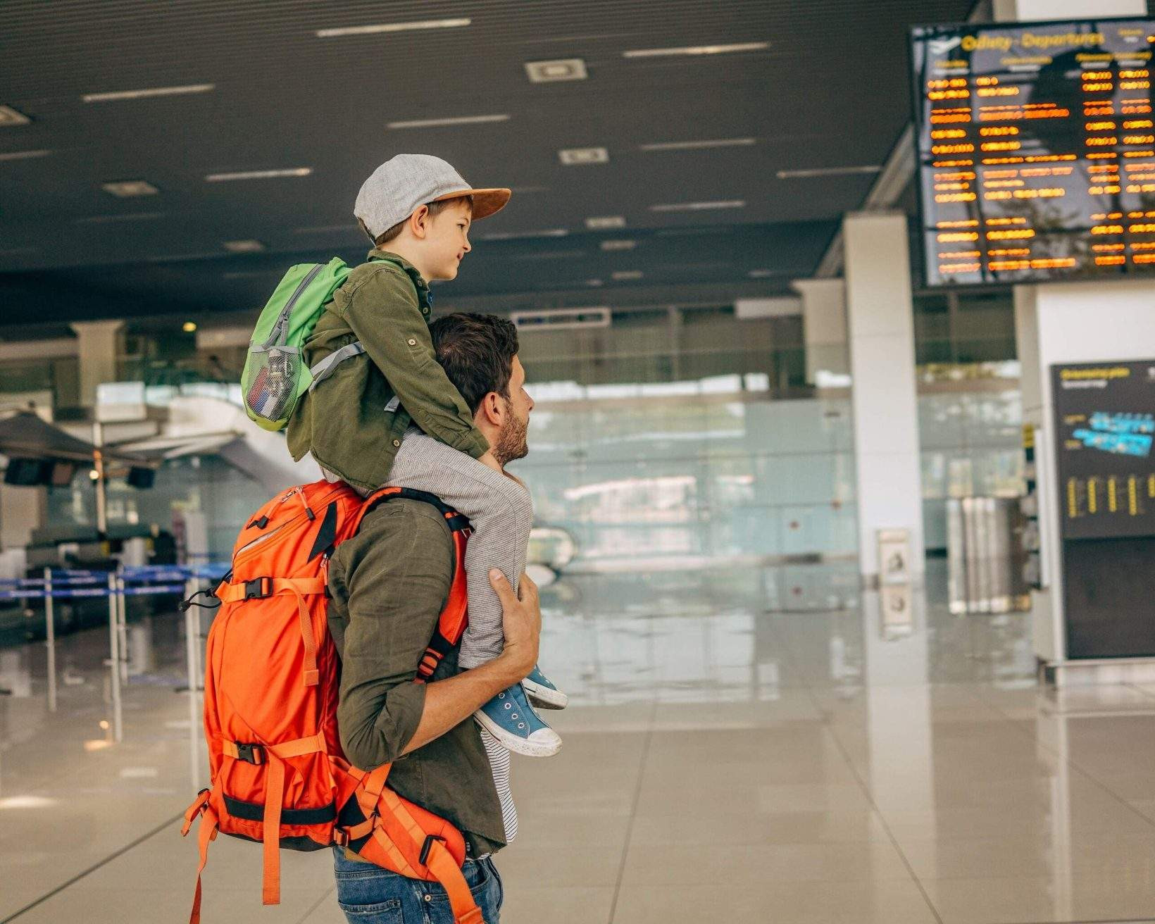 A father carrying his child on his shoulders while walking through an airport, ready for their flight.