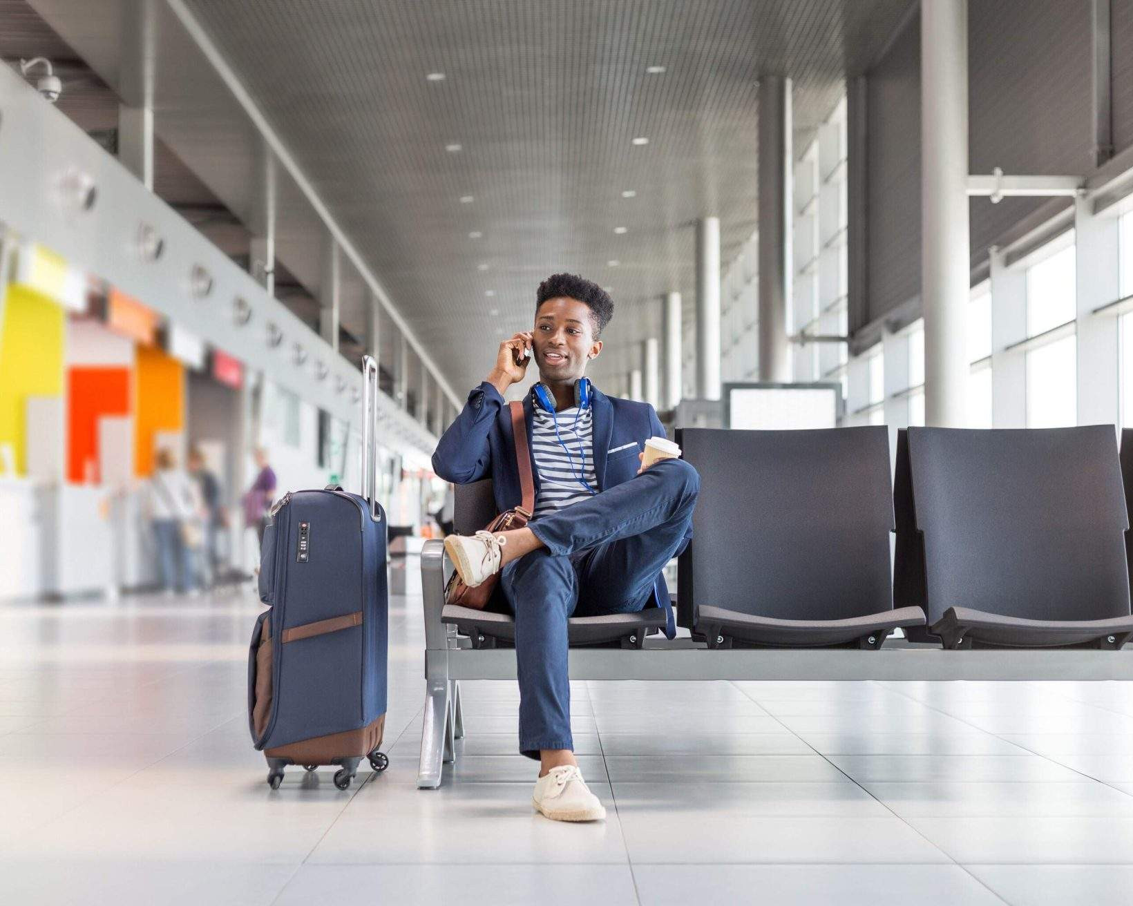 A traveler uses his smartphone in an airport lounge while waiting for his flight, possibly checking travel details or communicating with someone.