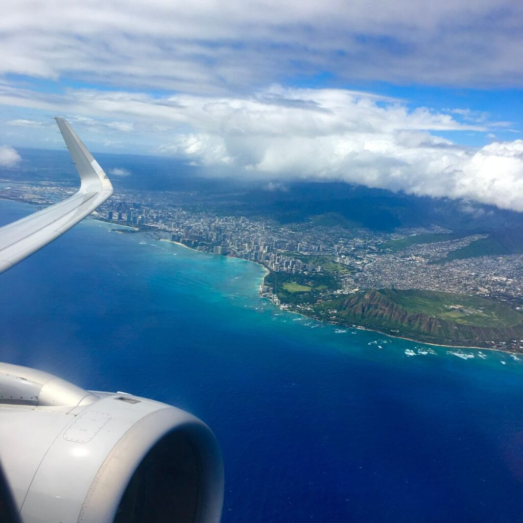 Aerial view from airplane window showcasing the ocean and clouds. This image illustrates the common experience of flying over the Pacific Ocean on the way to Hawaii, answering the query about flight duration.