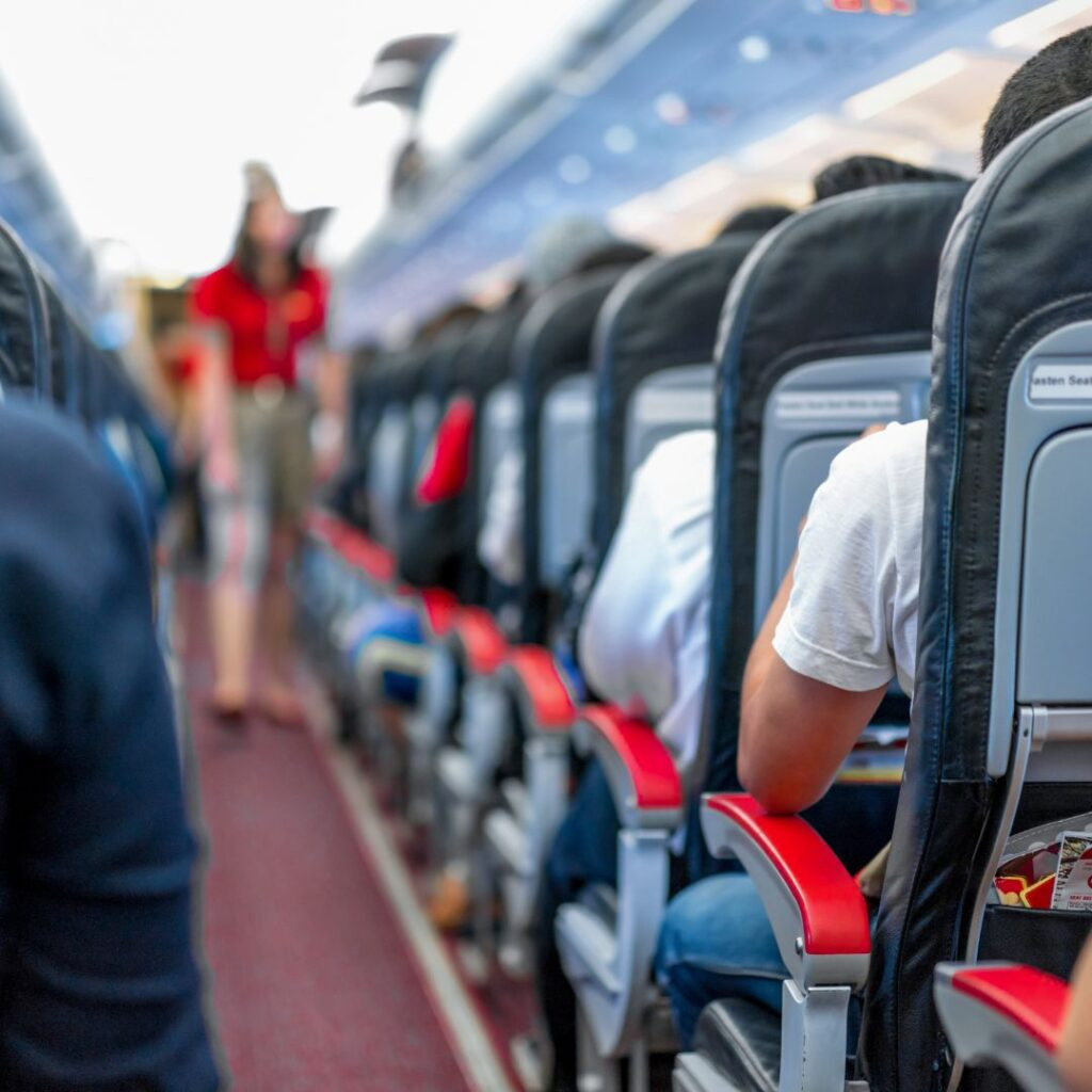 Interior of an airplane cabin, showing seats and overhead compartments. Passengers are seated, some are visible in the background. This image represents the flight experience and relates to the topic of flight duration to Hawaii.