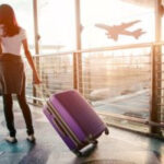 Woman pulling suitcase through airport terminal, wondering if it is safe to fly after wisdom teeth extraction