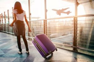 Woman pulling suitcase through airport terminal, wondering if it is safe to fly after wisdom teeth extraction