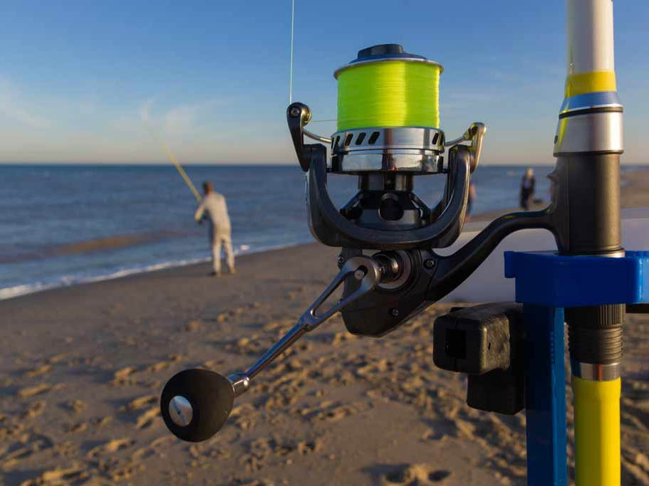 A close-up of a surf fishing rod, with a surf fisherman in the background.