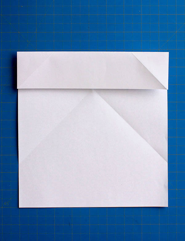 Step 5: Folding the top edge down to meet the first horizontal crease, forming the initial layer of the wings