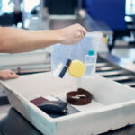 A traveler placing a clear plastic bag filled with travel-sized toiletries into a bin at an airport security checkpoint, adhering to TSA guidelines