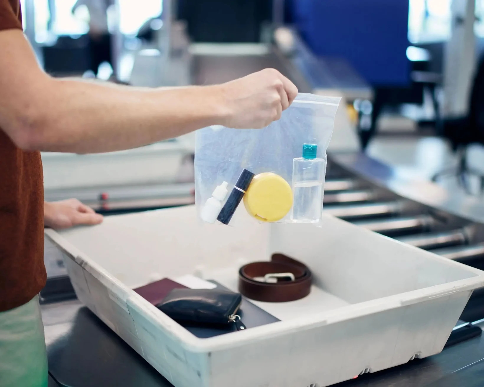 A traveler placing a clear plastic bag filled with travel-sized toiletries into a bin at an airport security checkpoint, adhering to TSA guidelines