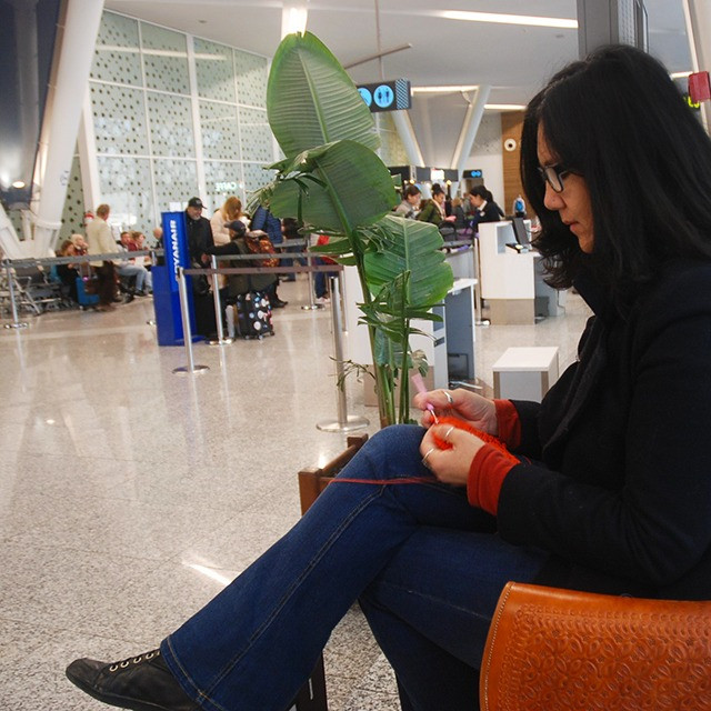 Woman crocheting on a plane with her feet up and sipping coffee