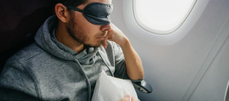 Man resting on a plane with a sleep mask.