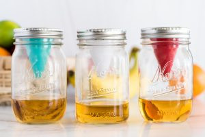 Three mason jars, each with a fruit fly funnel. One red, one white and one teal