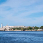 A view of the lighthouse on the ocean in Havana underneath a blue sky.