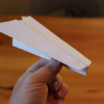 A hand launching a paper airplane outdoors, showcasing the throwing technique.