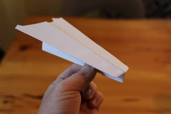 A hand launching a paper airplane outdoors, showcasing the throwing technique.