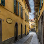Narrow street flanked by yellow buildings in the town of Bellagio - Lake Como, Italy - rossiwrites.com