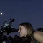 A person looking through a telescope pointed at the sky at night.