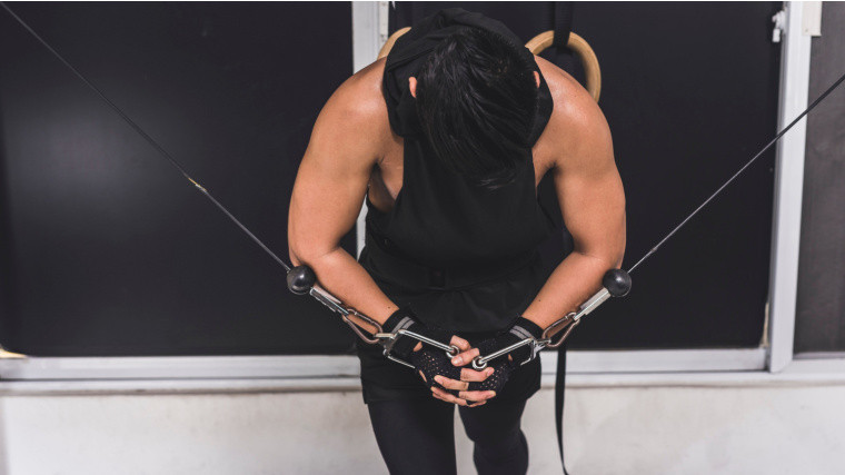 A person in a gym doing cable flye with poor form