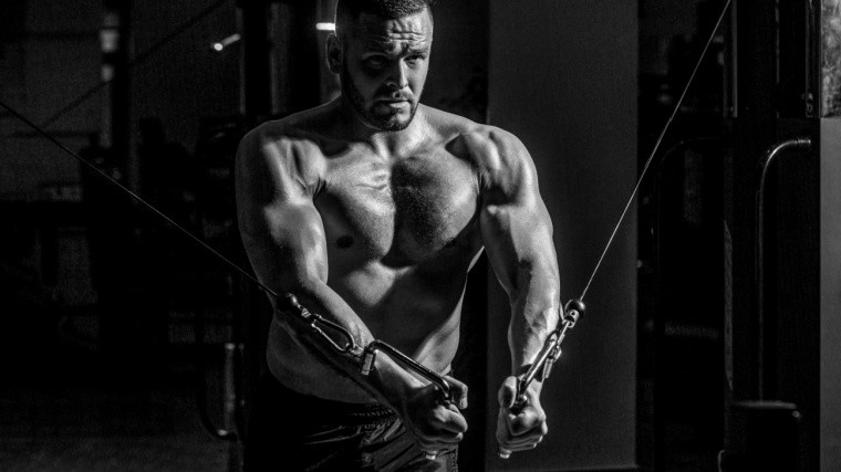 A muscular person in a gym performing a cable flye, highlighting lower chest development