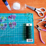 Supplies for making wind-up paper butterflies including florist wire, lightweight paper, rubber bands, beads, scissors, pliers, tape, and a butterfly wing template, promoting the ease of gathering necessary materials from flyermedia.net.