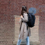 Spirit Airlines passenger wearing a trench coat and carrying a black backpack that fits Spirit Airlines personal item dimensions