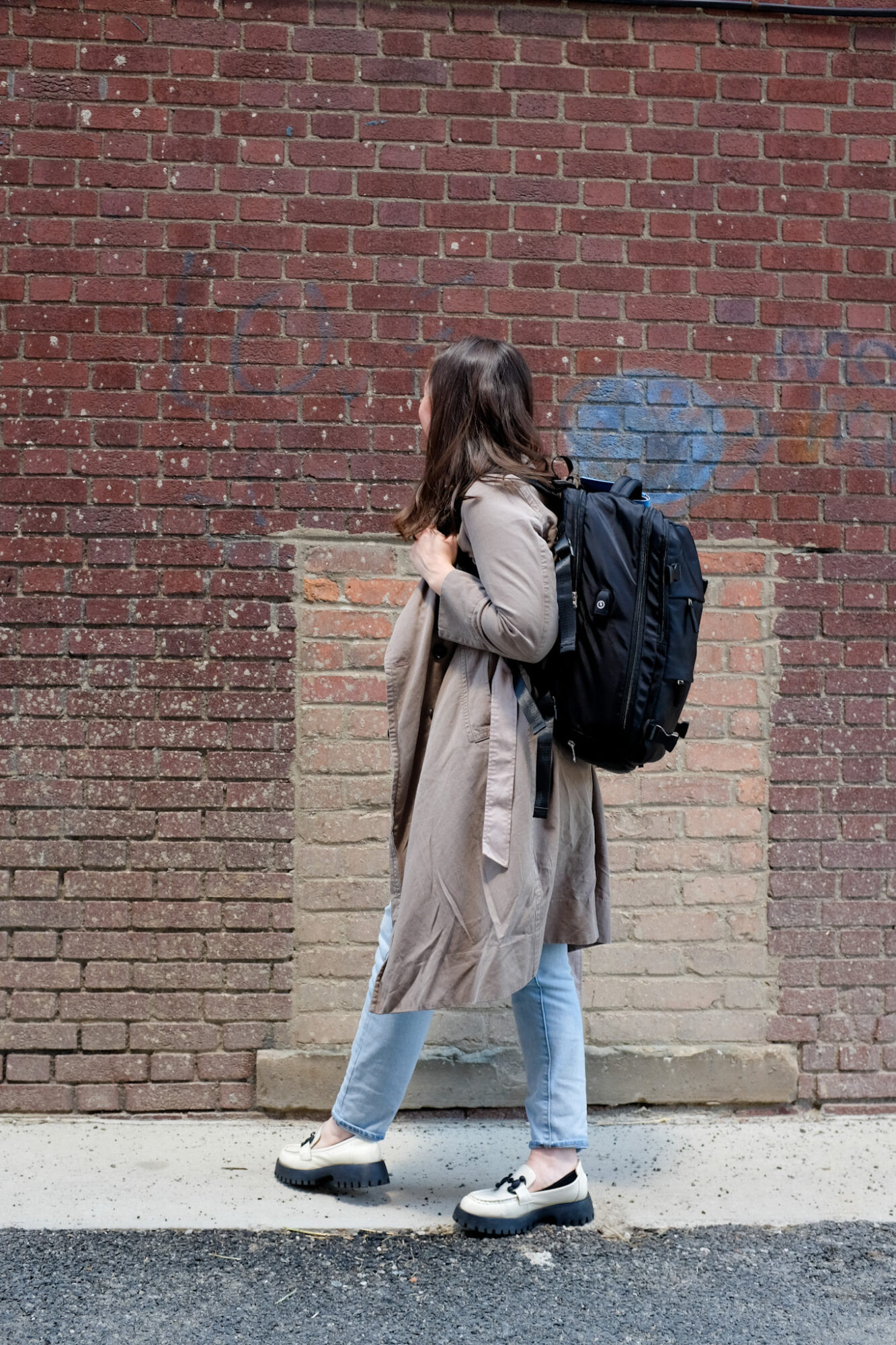 Spirit Airlines passenger wearing a trench coat and carrying a black backpack that fits Spirit Airlines personal item dimensions