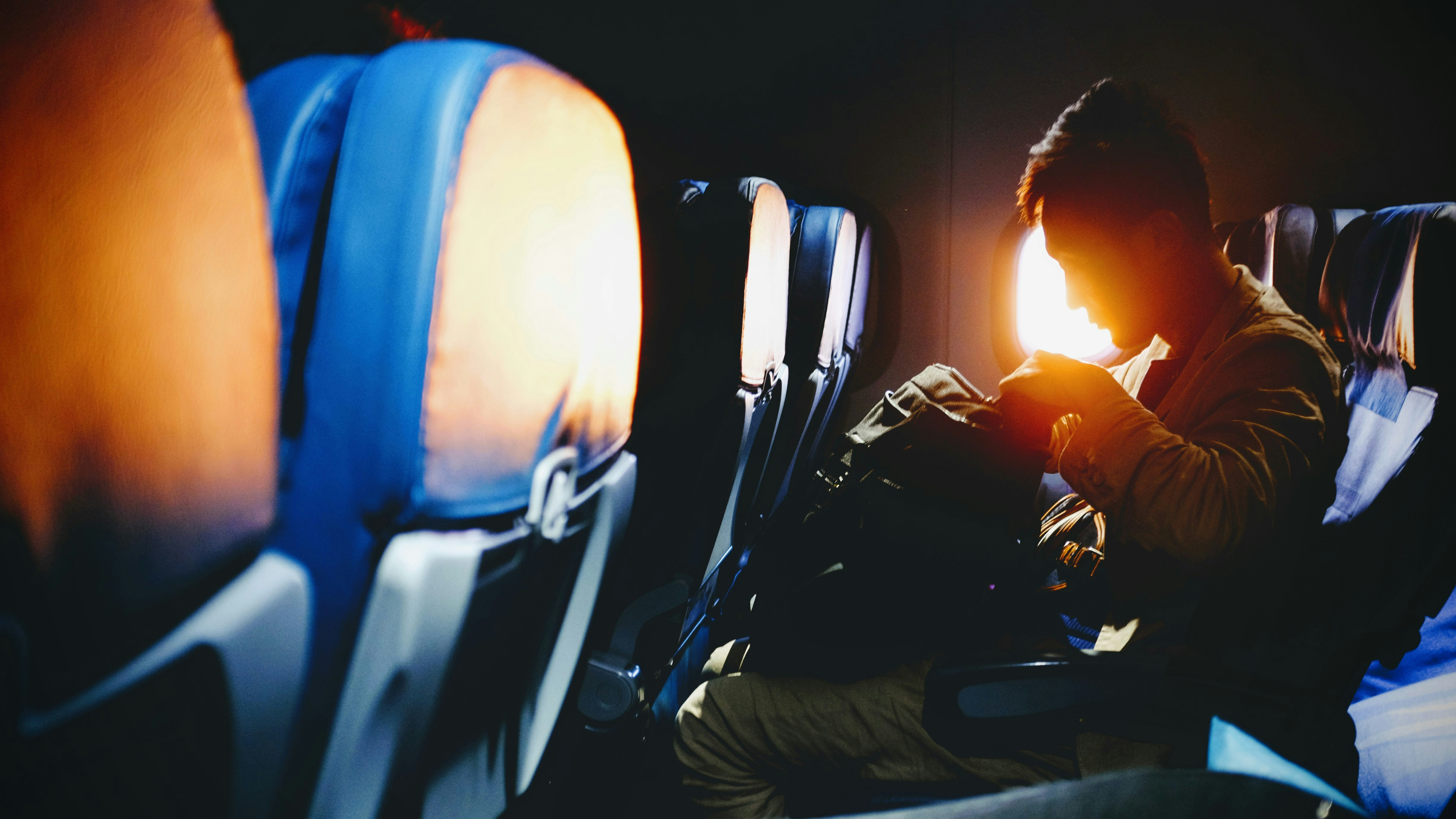 Man looking in his bag sitting on plane seat from Bambi Corro. The man is searching for the nicotine pouches to get rid of nicotine craving